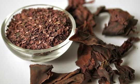 Bowl of dried reddish seaweed beside larger dried seaweed pieces