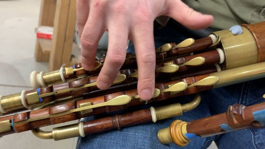 Close-up of wooden uilleann pipes with brass keys under a player's hand